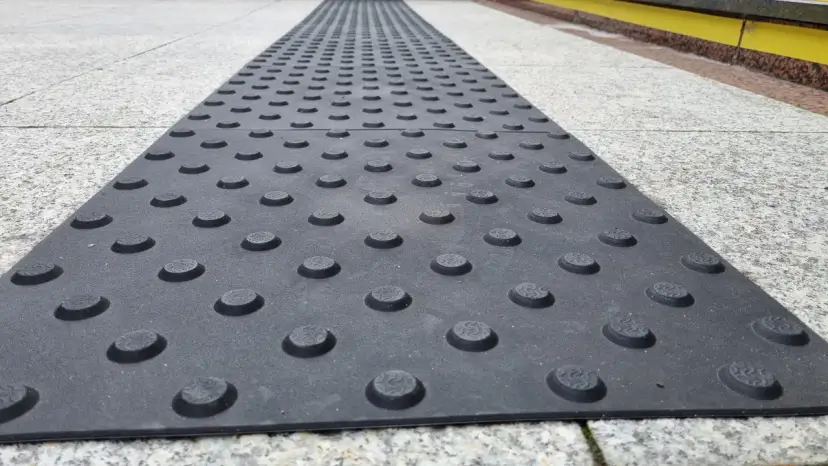 Czarna płyta z wypukłymi guzikami na szarym chodniku.