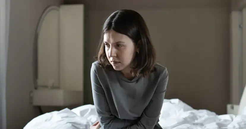 Smutna młoda kobieta siedzi na łóżku, patrząc w dół.