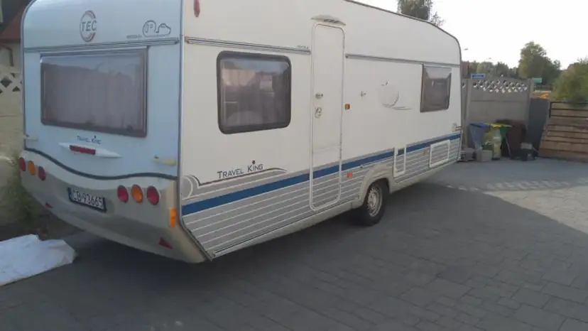 Biała przyczepa kempingowa TEC Travel King z niebieskimi pasami, gotowa na wakacyjne podróże.