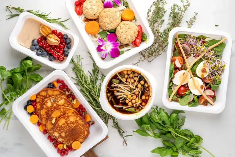 Pięć białych pojemników z różnorodnymi zdrowymi posiłkami, owocami i ziołami.