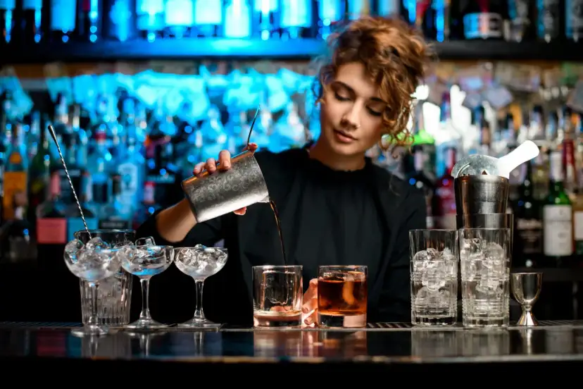 Barman nalewa drink do szklanki na tle butelek i niebieskiego światła.