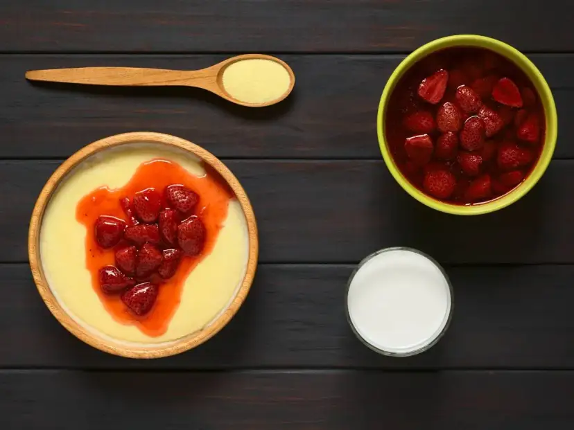 Grysik, czyli kasza manna, z truskawkami i musem. Obok miseczka z truskawkami w syropie i szklanka mleka.