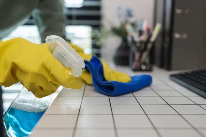 Ręka w żółtej rękawiczce rozpyla płyn na kafelki, obok leży ściereczka.