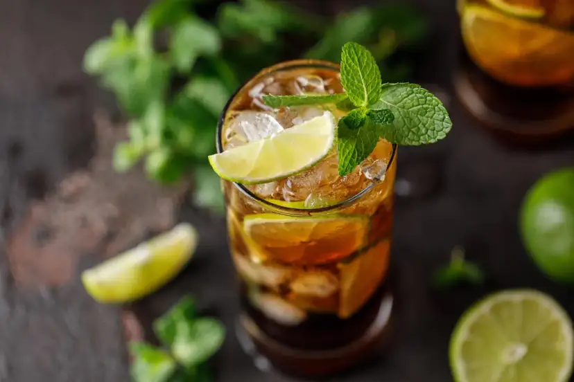 Szklanka z drinkiem Cuba Libre, lodem, plasterkami limonki i miętą.