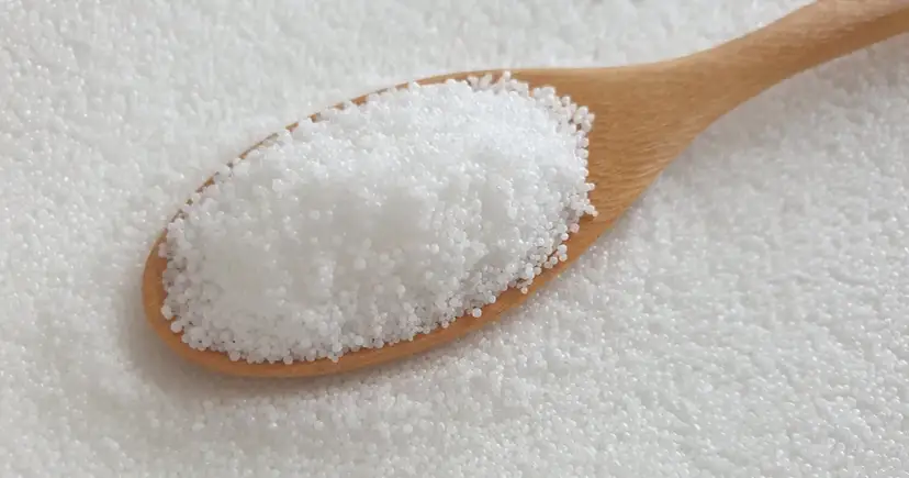 Drewniana łyżka pełna białych granulek. To stearyna, składnik świec i kosmetyków.