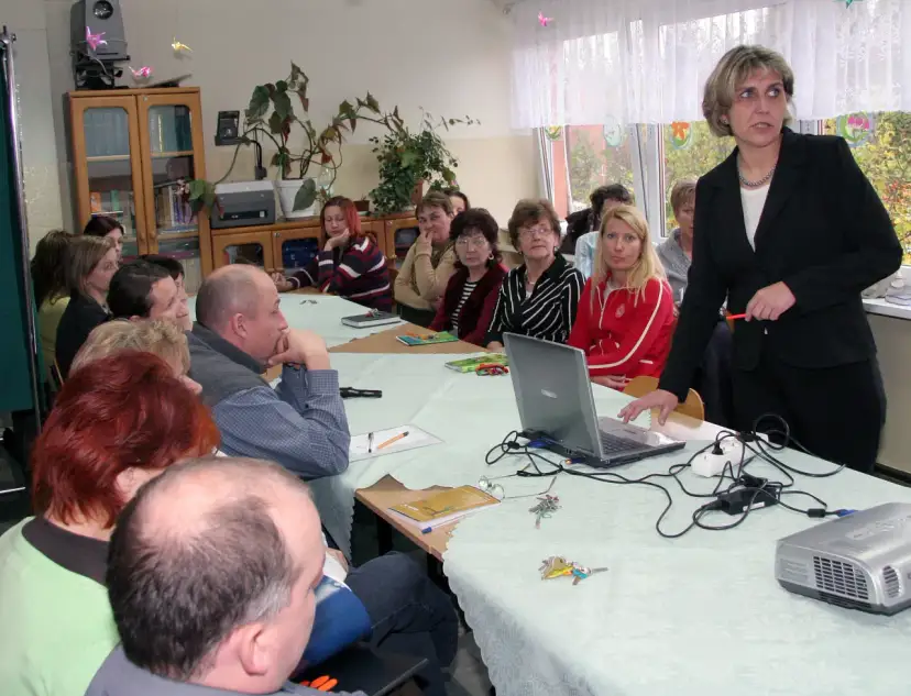 Nauczyciele zebrani na radzie pedagogicznej, dyskutują przy stole z laptopem i projektorem.