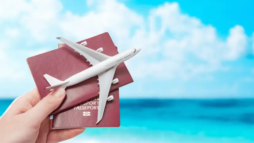 Dłoń trzyma paszporty z modelem samolotu na tle błękitnego nieba i morza.