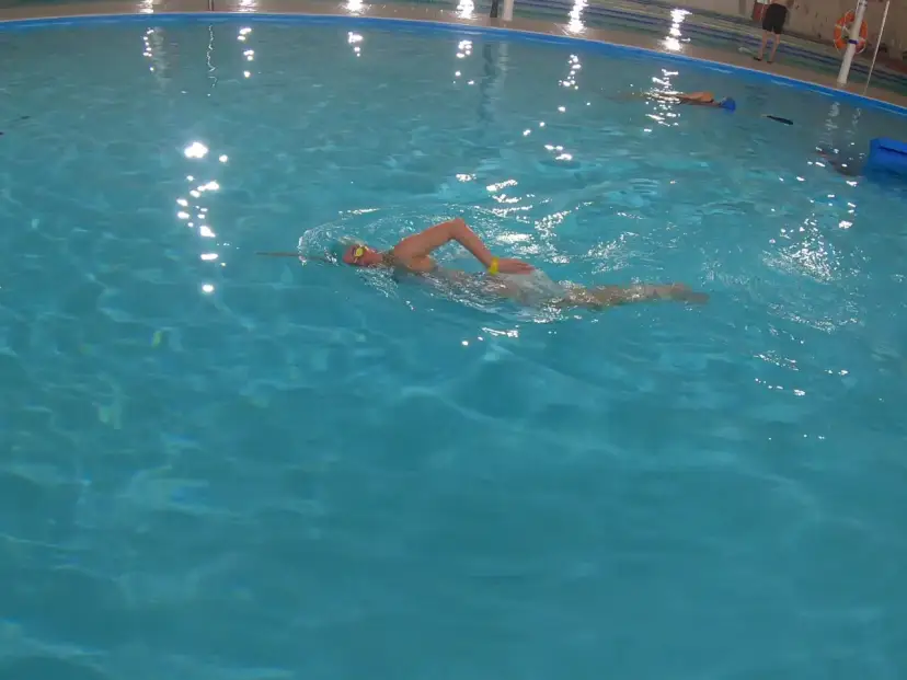 Osoba w czepku i okularach pływa kraulem. To świetny przykład, jak zacząć naukę pływania.