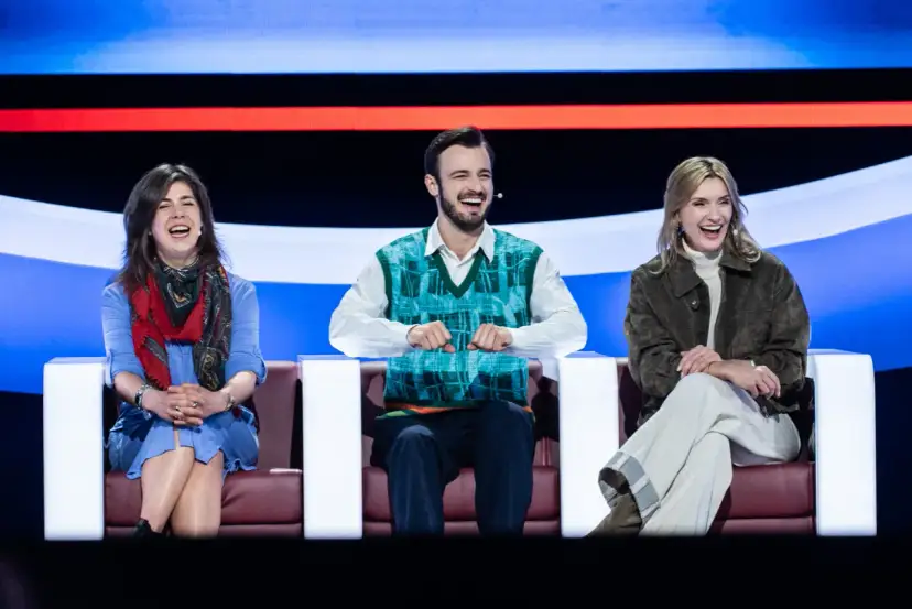 Trzy osoby śmieją się na kanapie, jakby oglądali koło fortuny kiedy w tv.