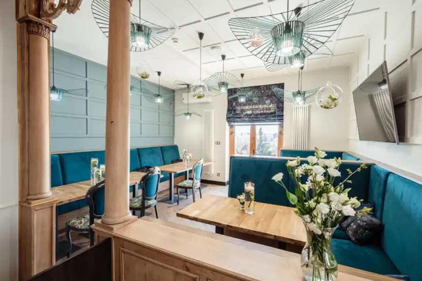 Wnętrze restauracji z turkusowymi kanapami, drewnianymi stołami i ozdobnymi lampami.