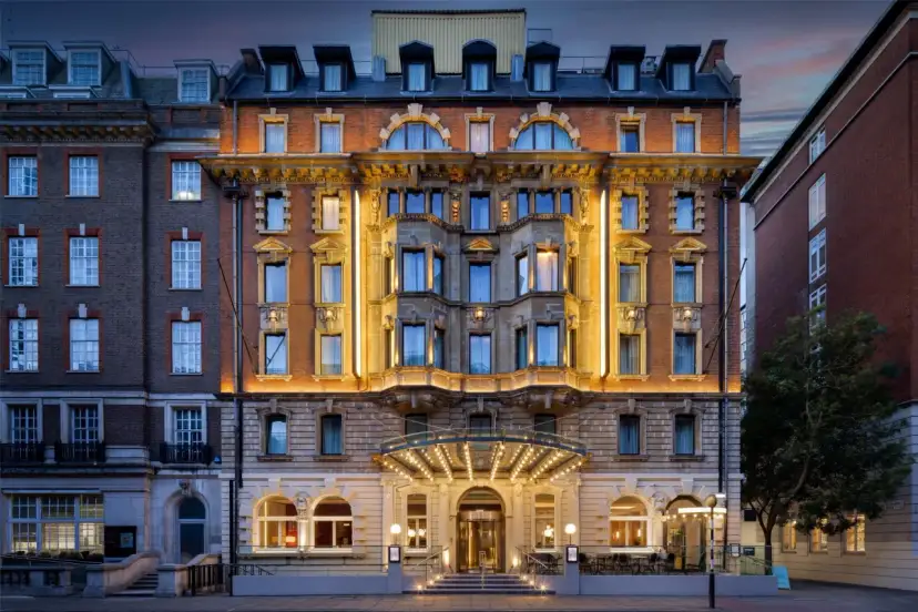 Elegancki hotel w Londynie z oświetloną fasadą i wejściem, nocą.