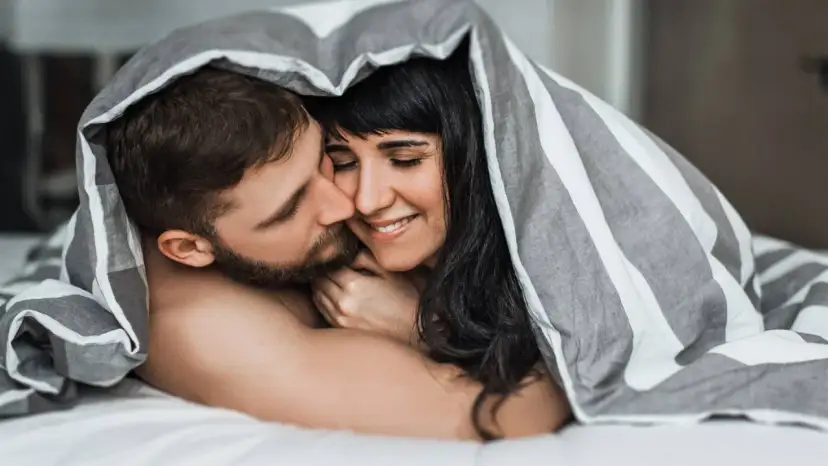 Para, przytuleni pod kołdrą, czule całujący się. Idealna randka do łóżka.