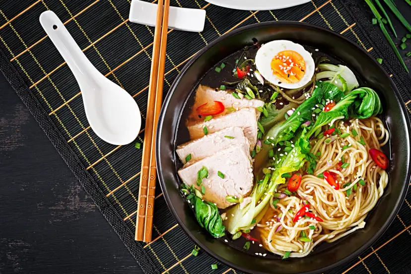 Miseczka ramenu z plastrami wieprzowiny, jajkiem na twardo, warzywami i makaronem. Dodatki do ramenu, takie jak szczypiorek i sezam, podkreślają smak.