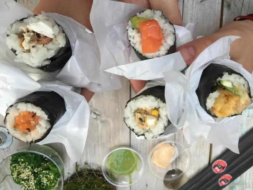 Ręcznie robione handroll sushi z łososiem, awokado, tuńczykiem i krewetkami. Pyszne przekąski na drewnianym stole.