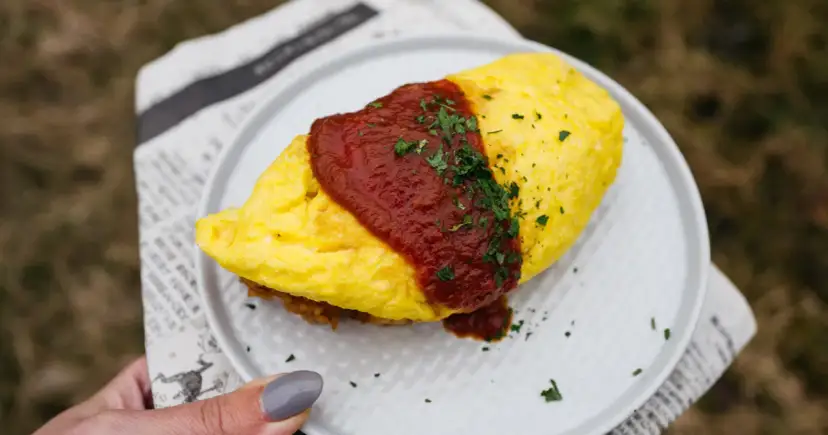 Pyszny omlet ryżowy polany sosem pomidorowym i posypany natką pietruszki, podany na talerzu.
