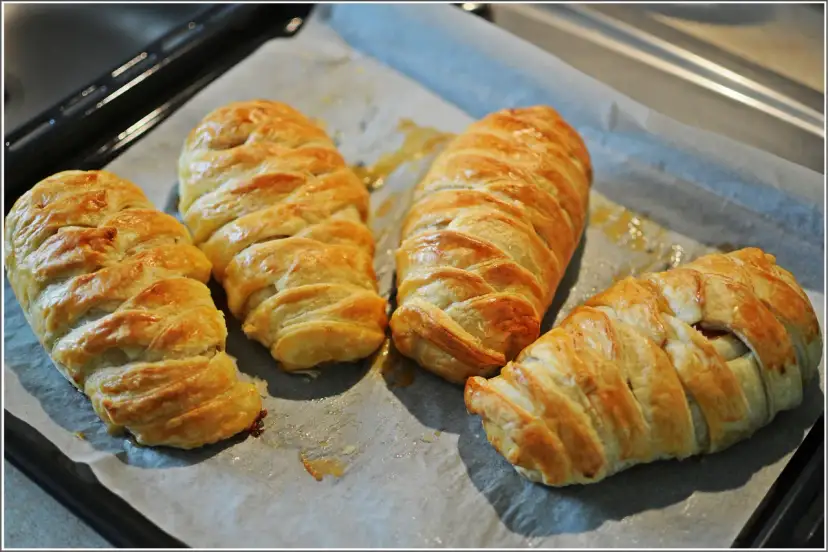 Cztery złociste kurczaki w cieście francuskim, upieczone na blasze, wyglądają apetycznie.