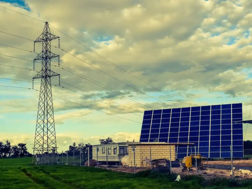 Własny prąd bez podłączenia do sieci: duża farma fotowoltaiczna obok wieży energetycznej i przyczepy mieszkalnej.