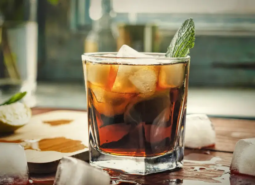 Orzeźwiający gin z colą, z lodem i listkiem mięty, na drewnianym blacie. Idealny na letnie popołudnie.