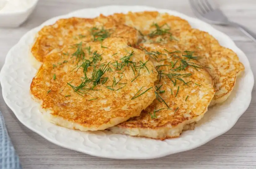 Placki ziemniaczane posypane koperkiem na białym talerzu.