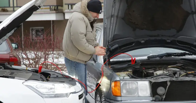 Mężczyzna podłącza kable rozruchowe do samochodu, by odpalić toyotę hybrydę na kable.