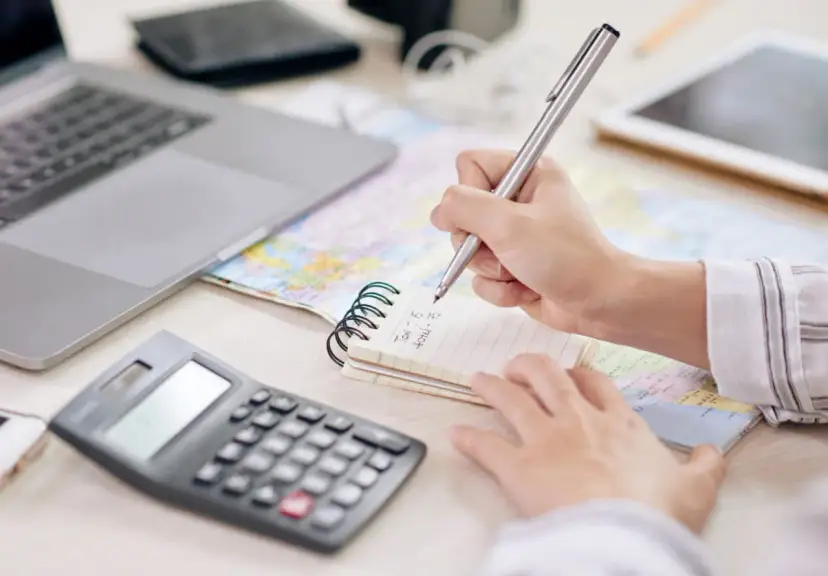 Osoba notuje na zeszycie, jak obliczyć odsetki od pożyczki prywatnej, obok leży kalkulator i laptop.