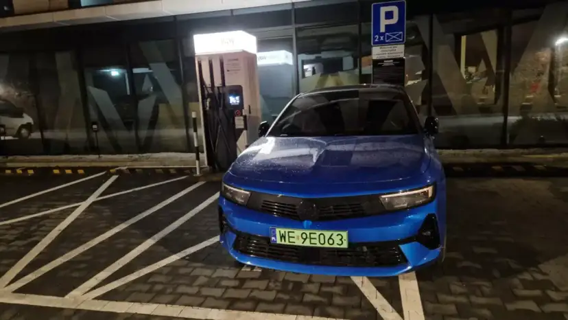 Niebieski samochód elektryczny pod ładowarką. Zastanawiasz się, ile się płaci za ładowanie samochodu elektrycznego?