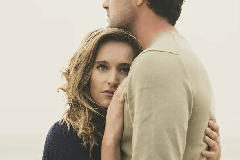 Blondynka wtulona w ramiona mężczyzny. Jej spojrzenie sugeruje, że wie, jak uwodzić kobietę, czując się bezpiecznie i pożądana.