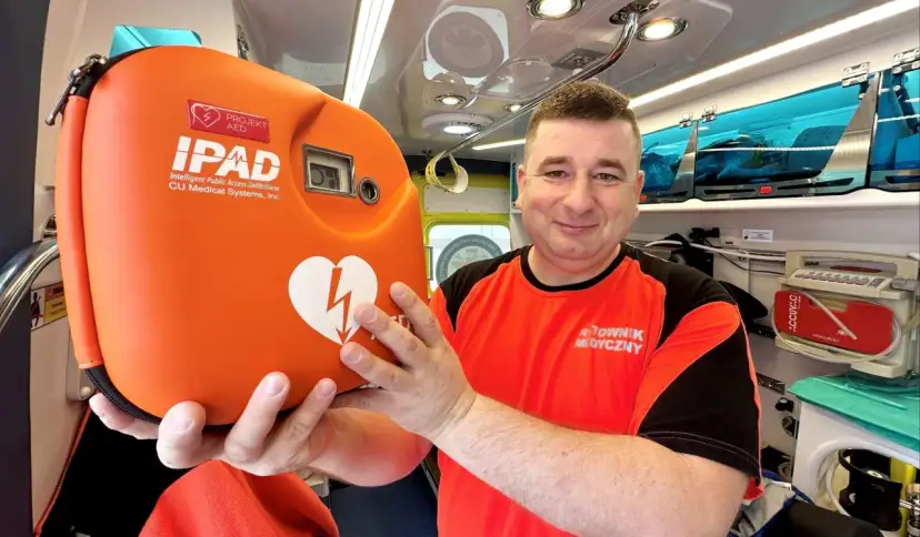 Ratownik medyczny trzyma pomarańczowy defibrylator AED w karetce.