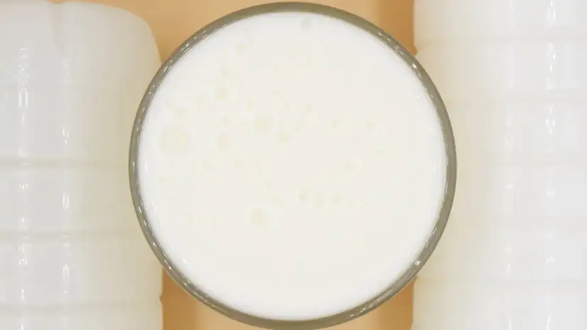 Szklanka pełna pianistego kefiru, otoczona białymi butelkami. Idealny moment, kiedy pić kefir, to teraz!