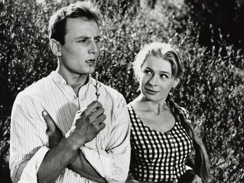 Młody mężczyzna, Eugeniusz Korczarowski, z gałązką w ustach, spogląda w bok. Obok niego uśmiechnięta kobieta w kratkę.