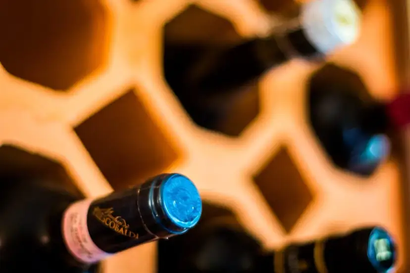 Wino w butelkach leżakuje w drewnianym stojaku. Prawidłowe przechowywanie wina w butelkach zapewnia jego jakość.