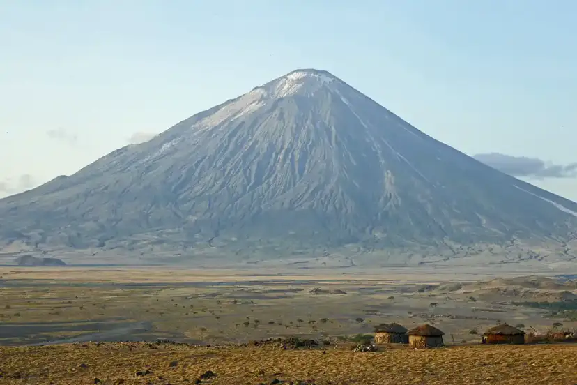 Ol Doinyo Lengai, wulkan w Tanzanii, góruje nad sawanną z kilkoma tradycyjnymi chatami Masajów.