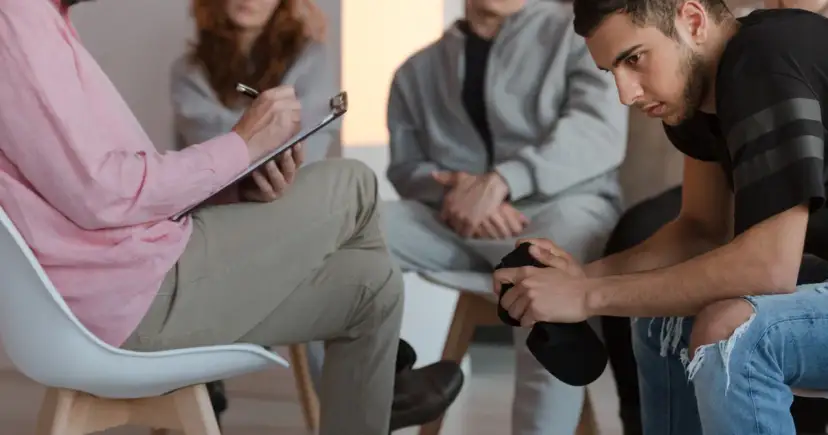 Grupa ludzi na sesji terapeutycznej, jedna osoba notuje.