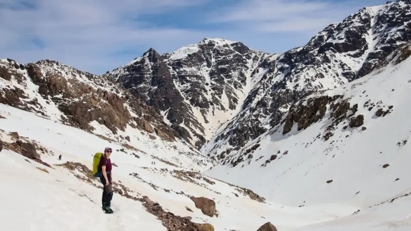 Wspinaczka na najwyższy szczyt Maroko, Toubkal. Widok na ośnieżone góry i turystkę z plecakiem.