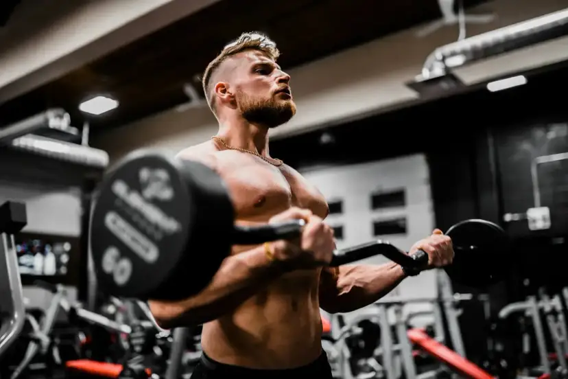 Mężczyzna ćwiczy biceps z ciężarem, wiedząc, że shake proteinowy co daje dla mięśni.