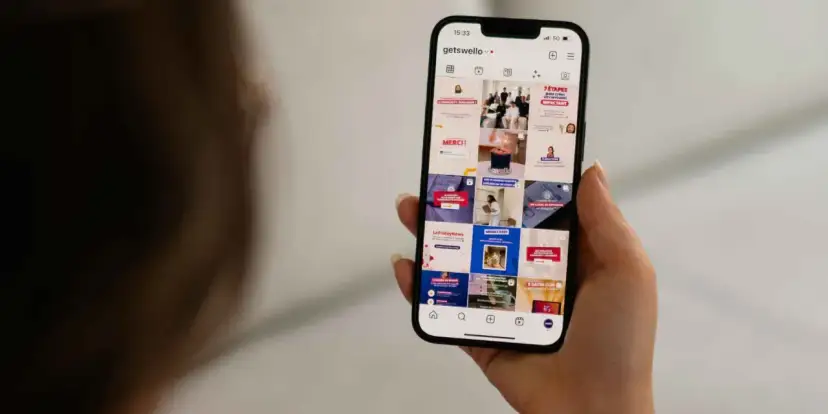 Dłoń trzyma smartfon z widokiem profilu Instagram z różnymi postami.