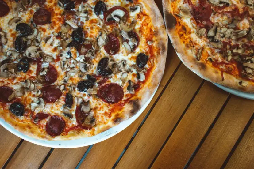 Dwie pizze z bogactwem składników na wierzchu: salami, pieczarki i czarne oliwki. Idealne na wspólny posiłek.