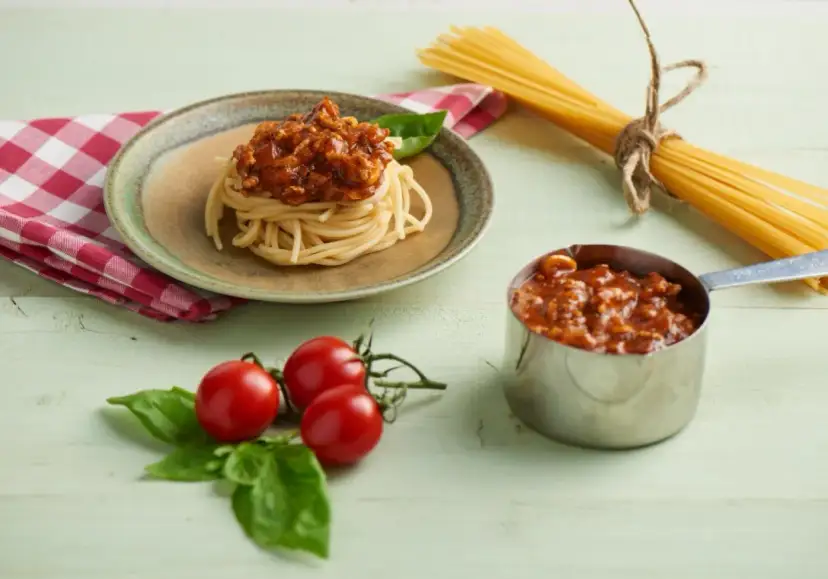 Pyszny sos do spaghetti z mięsem mielonym, podany na talerzu z makaronem, obok świeżych pomidorków i bazylii.