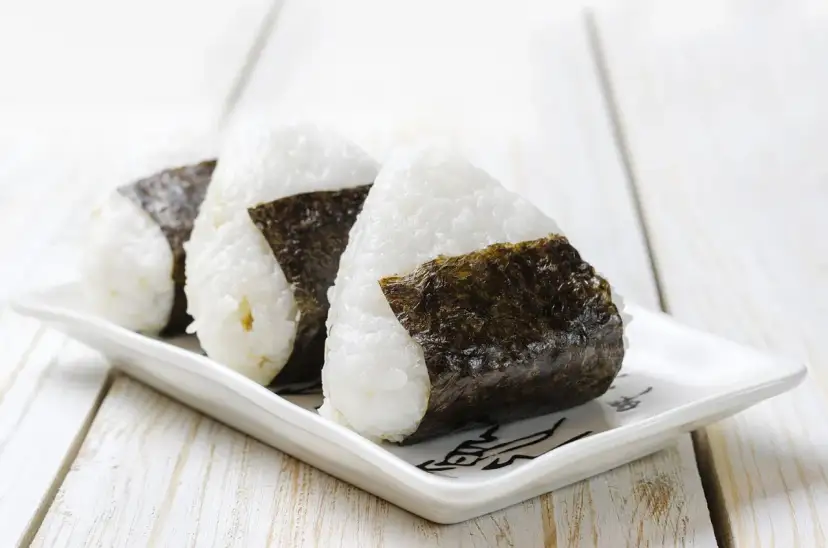 Trzy ryżowe kulki onigiri z nori na białym talerzyku. Idealne na szybki lunch, oto prosty onigiri przepis.