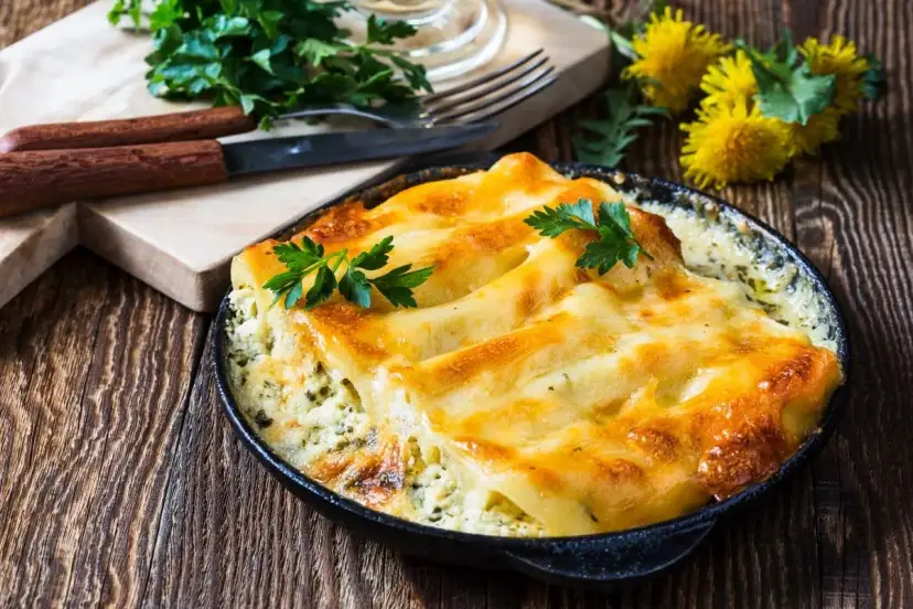Złociste, zapieczone makaron cannelloni w sosie, udekorowane natką pietruszki, na drewnianym stole.