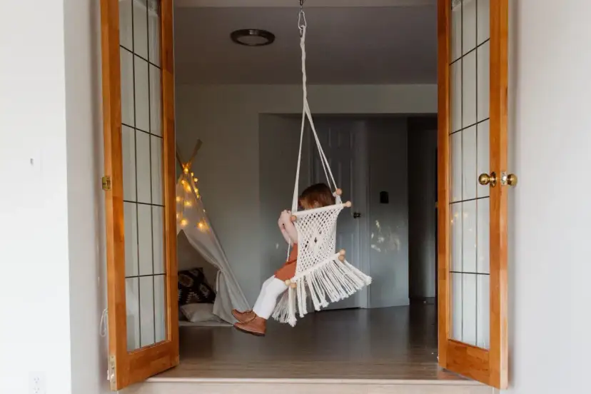 Dziecko buja się na huśtawce z makramy, wiszącej w futrynie. Pomysł na to, jak zamontować huśtawkę w futrynie.
