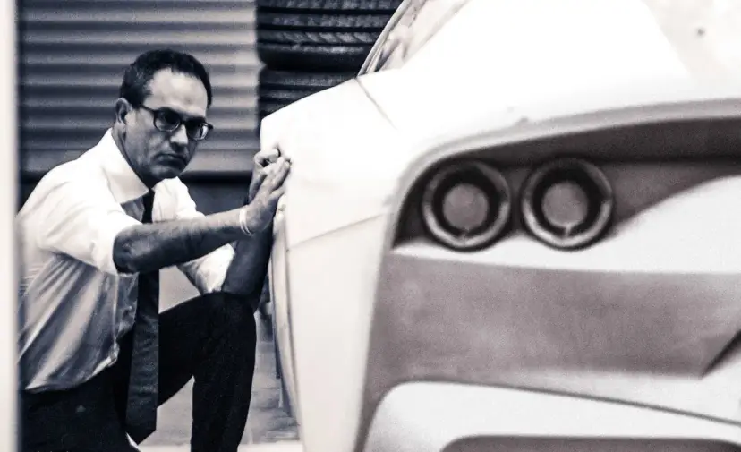 Mężczyzna w okularach i białej koszuli dopracowuje kształt prototypu, który przypomina, jak wygląda Ferrari.