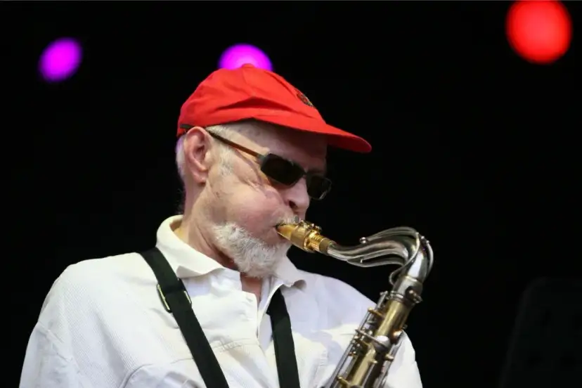 Starszy mężczyzna w czerwonej czapce i okularach gra na saksofonie.