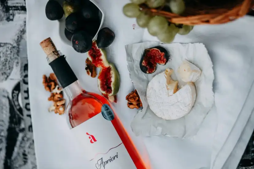 Butelka różowego wina, ser pleśniowy, figi i orzechy włoskie na białym obrusie.