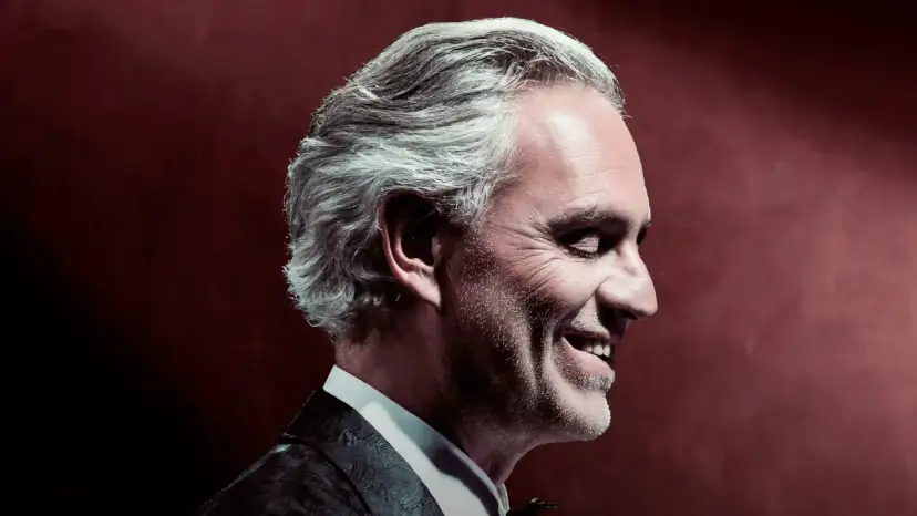 Uśmiechnięty Andrea Bocelli w garniturze, z siwymi włosami, w profilu. To zapowiedź, gdzie koncert Bocellego.