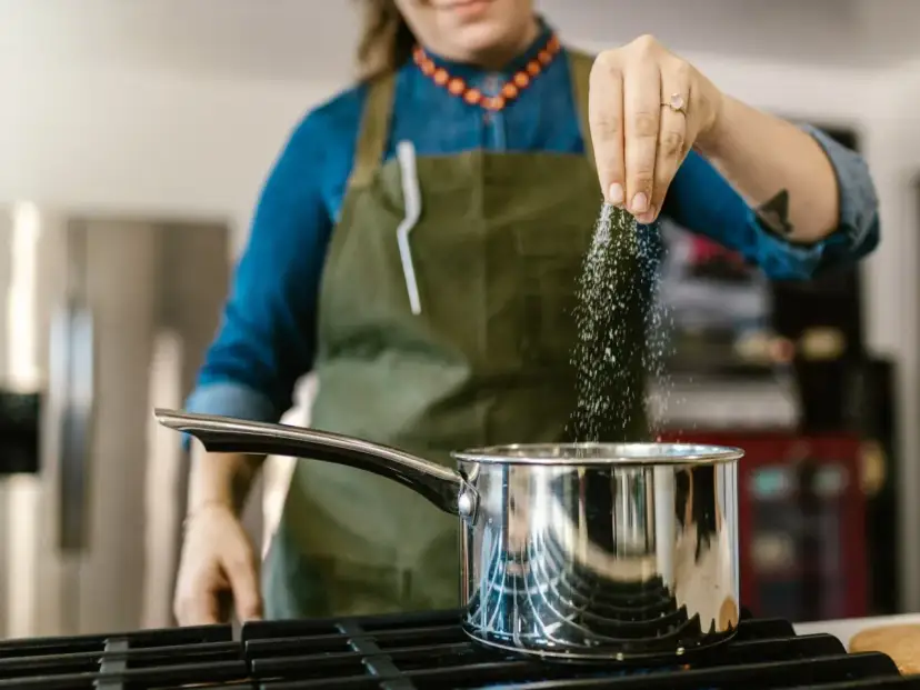 Kobieta w fartuchu dodaje sól do garnka, zastanawiając się, ile sodu dziennie jest bezpieczne.