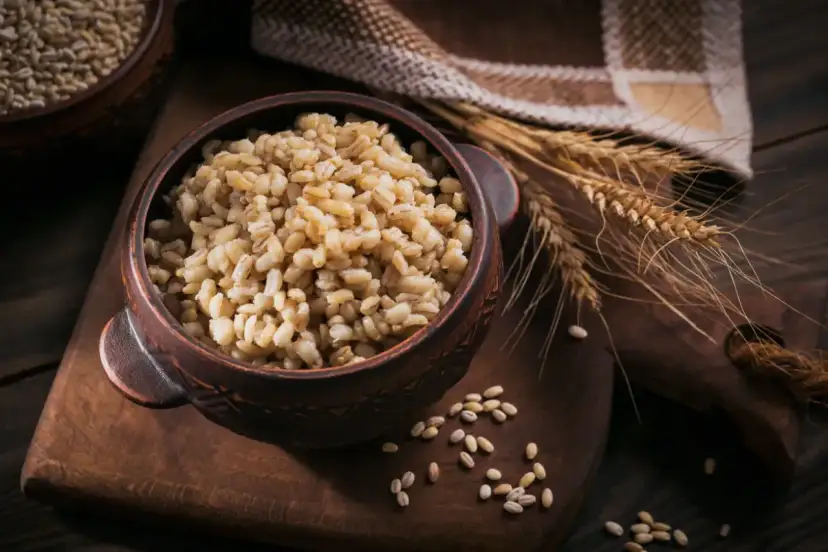 Miseczka pełna kaszy jęczmiennej, która ma niski indeks glikemiczny. Obok kłosy zbóż i lniany ręcznik.