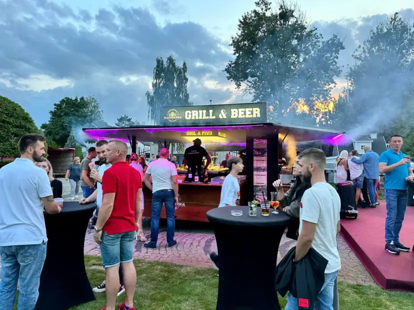 Ludzie przy stoisku z grillem i piwem, dym i fioletowe światła.