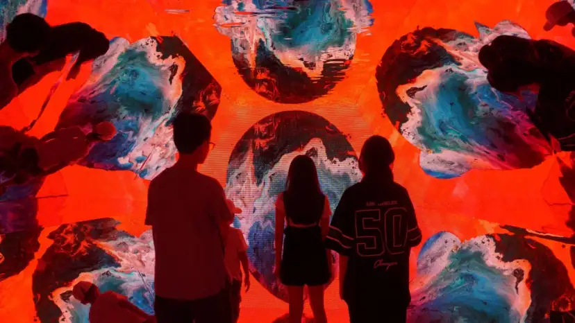 Ludzie patrzą na abstrakcyjną, kolorową instalację świetlną z dominującym czerwonym tłem.