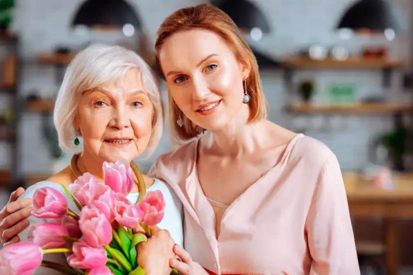 Dwie kobiety, matka i córka, uśmiechają się, trzymając bukiet różowych tulipanów. Wiersz "serce matki" idealnie oddaje ich więź.
